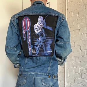 May include: A denim jacket and matching jeans. The jacket features a large patch on the back with the text "Ozzy Osbourne" and an illustration of a musician. The jeans have a classic five-pocket design.