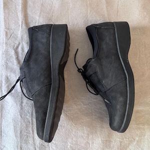 Op de afbeelding: Een paar zwarte leren schoenen met veters. De schoenen hebben een ronde neus en een dikke zool. Het leer heeft een textuur. De schoenen zijn ontworpen voor comfort en dagelijks gebruik.