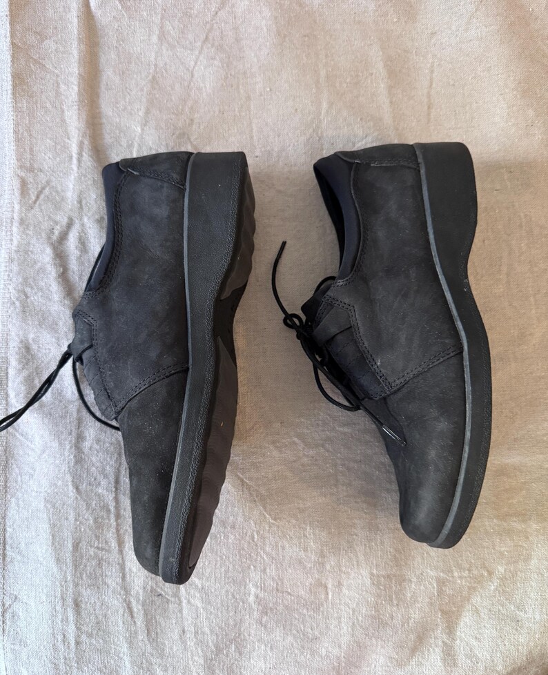 Op de afbeelding: Een paar zwarte leren schoenen met veters. De schoenen hebben een ronde neus en een dikke zool. Het leer heeft een textuur. De schoenen zijn ontworpen voor comfort en dagelijks gebruik.