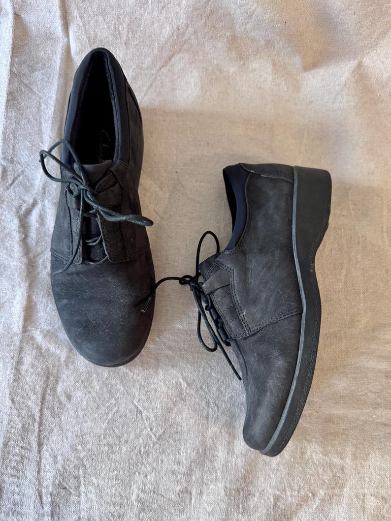 Op de afbeelding: Een paar zwarte veterschoenen. De schoenen hebben een ronde neus en een lage hak. De veters zijn zwart en vastgebonden. De schoenen zijn gemaakt van een su&egrave;de-achtig materiaal.