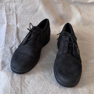 Op de afbeelding: Een paar zwarte su&egrave;de veterschoenen. De schoenen hebben een ronde neus en een lage hak. De veters zijn zwart en de schoenen lijken ongedragen. De schoenen worden gepresenteerd op een neutraal gekleurde stof.