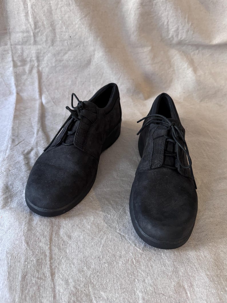 Op de afbeelding: Een paar zwarte su&egrave;de veterschoenen. De schoenen hebben een ronde neus en een lage hak. De veters zijn zwart en de schoenen lijken ongedragen. De schoenen worden gepresenteerd op een neutraal gekleurde stof.