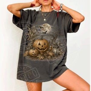 Könnte beinhalten: Ein anthrazitfarbenes Kurzarm-T-Shirt mit einem detaillierten Grafikdruck einer Halloween-Szene. Das Design zeigt geschnitzte Kürbisse, trockene Maisstängel, kahle Bäume, einen Vollmond und fliegende Fledermäuse in einer gedeckten, erdigen Farbpalette.