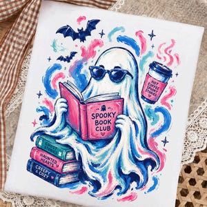 May include: A white rectangular print featuring a ghost wearing sunglasses and reading a pink book titled Spooky Book Club. The ghost sits atop a stack of books labelled Ghost Stories, Haunted Hearts, and Creepy & Cozy, with a coffee cup nearby.
