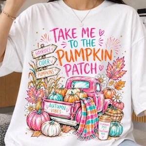 Könnte beinhalten: Ein weißes T-Shirt mit einer bunten Grafik eines pinken Pick-ups, der mit Kürbissen beladen ist. Der Text lautet Take me to the pumpkin patch und Autumn vibes. Das Design umfasst ein Holzschild, Herbstblätter und einen Kaffeebecher.
