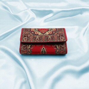 May include: A red wallet with a patterned design resembling a rug. The pattern is in shades of black, gold, and red.
