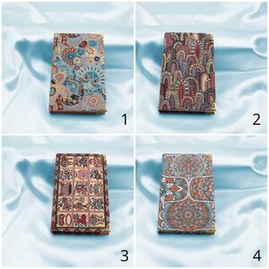 May include: Four different patterned fabric covered notebooks. The notebooks are all the same size and shape. The patterns are all colourful and intricate. The notebooks are arranged in a grid pattern.