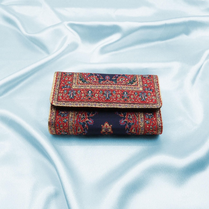 May include: A red, blue, and gold patterned wallet with a traditional rug design.