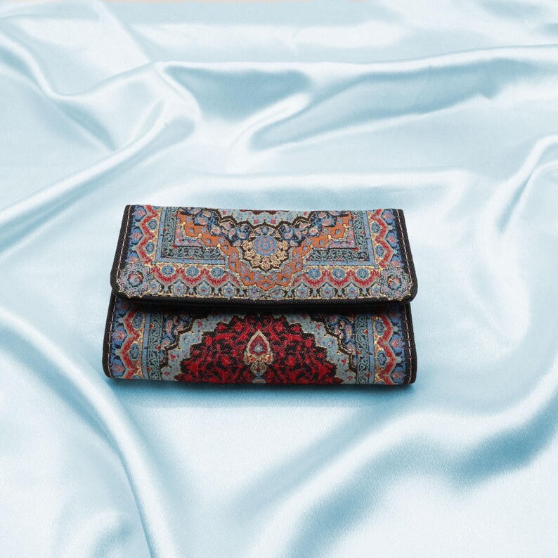 May include: A small, rectangular wallet with a colorful, intricate pattern. The wallet is made of a dark fabric with a black border and a red, blue, and gold design.