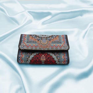 May include: A small, rectangular wallet with a colorful, intricate patterned design. The wallet is folded closed and has a black border.