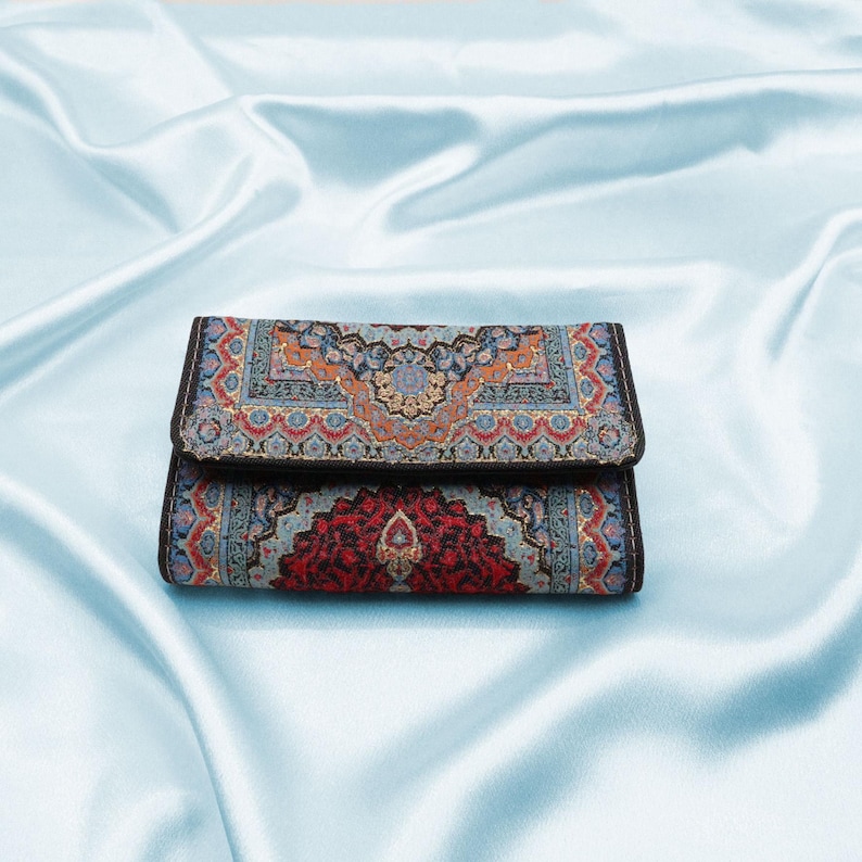 May include: A small, rectangular wallet with a colorful, intricate patterned design. The wallet is folded closed and has a black border.