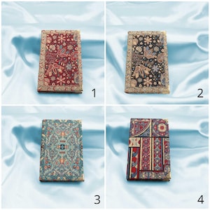 May include: Four different patterned notebooks with gold trim. The notebooks are on a light blue fabric background.