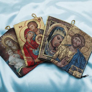 Könnte beinhalten: Vier kleine Wandteppichtaschen mit Reißverschluss. Jede Tasche zeigt ein anderes religiöses Symbol: die Heilige Familie, die Jungfrau Maria, Jesus Christus und einen Heiligen. Die Taschen sind aus weichem, gewebtem Stoff mit goldenen Akzenten.