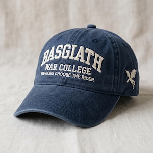 May include: A navy blue baseball cap with white embroidered text that reads "BASGIATH WAR COLLEGE DRAGONS CHOOSE THE RIDER." A white dragon emblem is embroidered on the side. The cap has a curved brim and a button on top.