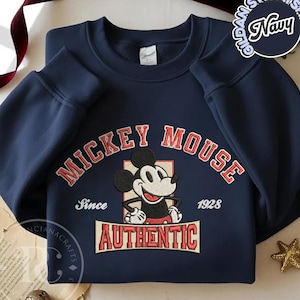 May include: Navy blue sweatshirt featuring a Mickey Mouse graphic. The design includes the words "MICKEY MOUSE" in red, "Since 1928", and "AUTHENTIC". The sweatshirt is a Gildan brand.