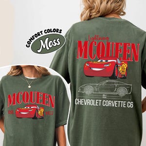May include: Moss green t-shirts featuring Lightning McQueen graphics. One shirt has "McQueen" in red, with a red car graphic and "EST. 1977". The other shirt has "Lightning McQueen" above a red car graphic and a Chevrolet Corvette C6 outline.