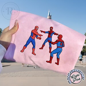 Puede incluir: Sudadera rosa claro con un dise&ntilde;o bordado de tres figuras de Spider-Man se&ntilde;al&aacute;ndose. Las figuras de Spider-Man visten sus trajes cl&aacute;sicos rojos y azules. La sudadera tiene la inscripci&oacute;n "Light Pink".