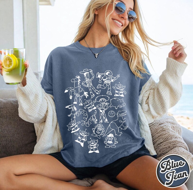 Puede incluir: Una camiseta azul con un dibujo lineal blanco de personajes de dibujos animados. La camiseta tiene un corte holgado y est&aacute; hecha de una tela suave. Las palabras "Blue Jean" est&aacute;n impresas en la esquina inferior derecha de la camiseta.