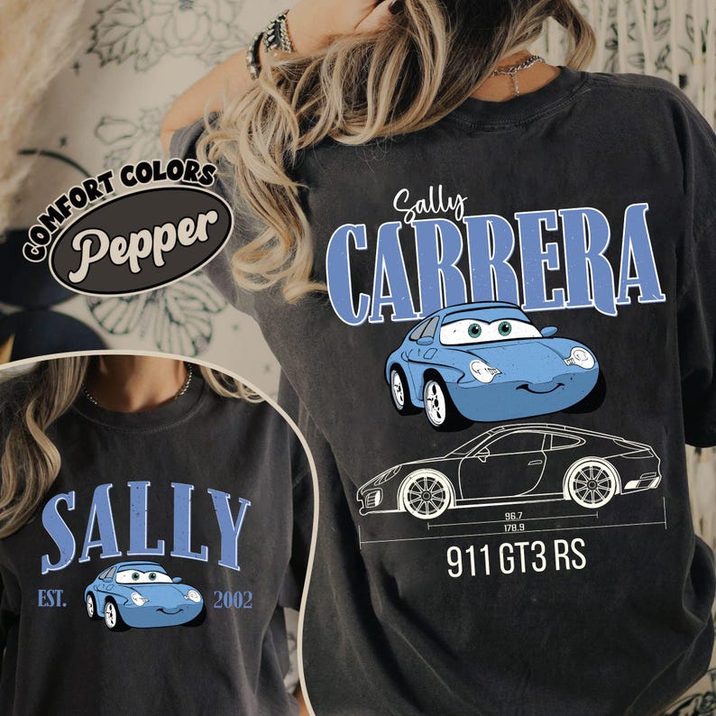 May include: Dark gray Comfort Colors t-shirt featuring the text "Sally Carrera" in blue, along with a cartoon image of a blue car. The shirt also includes a graphic of a car with dimensions and the text "911 GT3 RS".