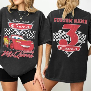 Może przedstawiać: Czarny t-shirt z grafiką Zygzaka McQueena z filmu Auta Disneya i Pixara. Prz&oacute;d zawiera logo Cars, szachownice i napis "Lightning McQueen". Tył ma dużą cyfrę 3 i napis "Custom Name".