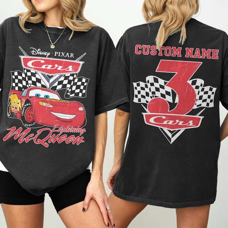 Może przedstawiać: Czarny t-shirt z grafiką Zygzaka McQueena z filmu Auta Disneya i Pixara. Prz&oacute;d zawiera logo Cars, szachownice i napis "Lightning McQueen". Tył ma dużą cyfrę 3 i napis "Custom Name".