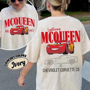 May include: Ivory-colored t-shirt featuring the text "MCQUEEN" and a red cartoon car graphic. The shirt also displays "EST. 1977" and "Lightning MCQUEEN" with a Chevrolet Corvette C6 schematic.