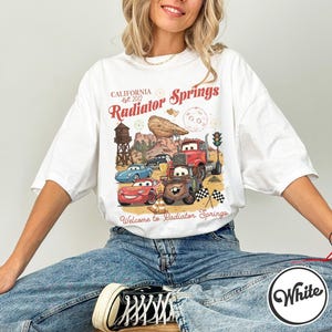 Pode incluir: Uma caneca de cer&acirc;mica branca com uma al&ccedil;a preta e o texto "But First, Coffee" em estilo manuscrito. A caneca est&aacute; sobre uma superf&iacute;cie branca. A caneca tem aproximadamente 10 cm de altura.