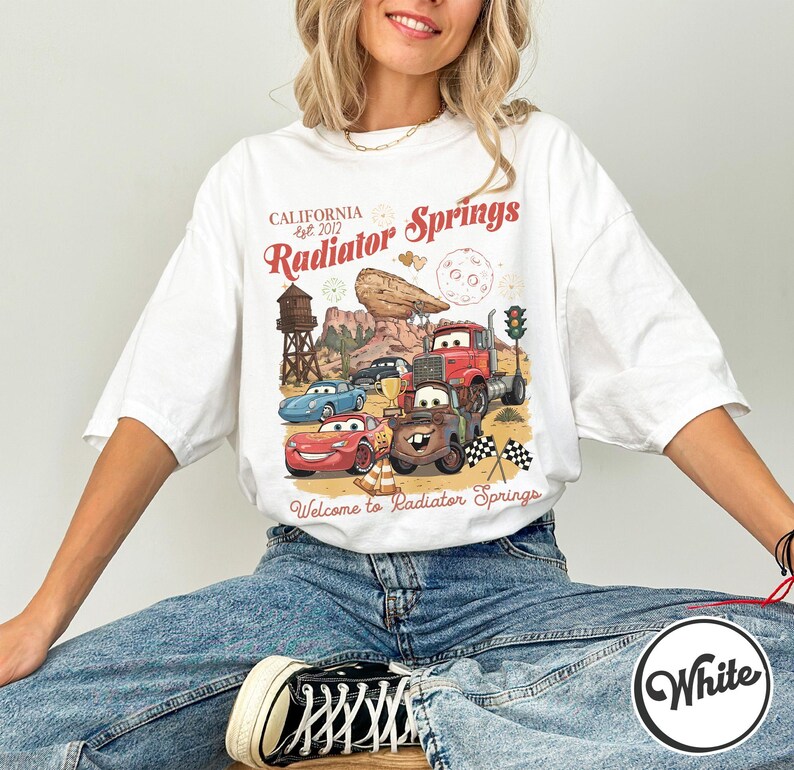 Pode incluir: Uma caneca de cer&acirc;mica branca com uma al&ccedil;a preta e o texto "But First, Coffee" em estilo manuscrito. A caneca est&aacute; sobre uma superf&iacute;cie branca. A caneca tem aproximadamente 10 cm de altura.