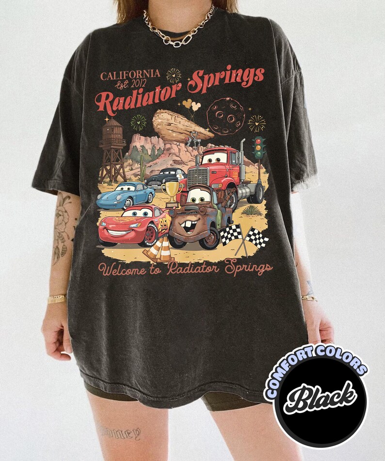Pode incluir: Camiseta preta com um gr&aacute;fico dos personagens do filme Carros e o texto "California Est. 2012 Radiator Springs Welcome to Radiator Springs." A camisa &eacute; da marca Comfort Colors.