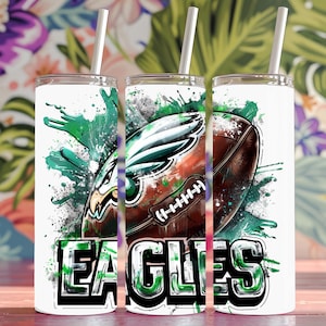 Może przedstawiać: Biały kubek z zielonym, czarnym i brązowym wzorem akwarelowym piłki nożnej i orła z napisem "EAGLES" w zielonych i czarnych literach.
