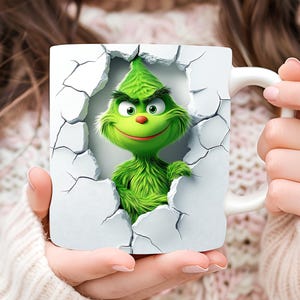May include: A white ceramic mug with a green Grinch character breaking through the mug's surface. The Grinch is smiling with a mischievous expression.