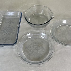 Puede incluir: Cuatro fuentes para hornear de vidrio transparente. Incluye una fuente rectangular con borde azul, un cuenco redondo con asas y dos moldes para tartas. Todos los platos tienen un patrón floral decorativo.