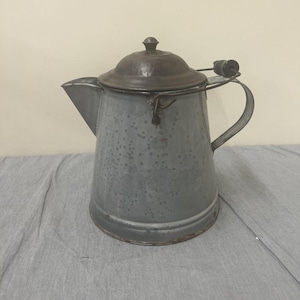 May include: A vintage gray metal pitcher with a lid and a handle. The pitcher has a speckled finish and a slightly rusted appearance.