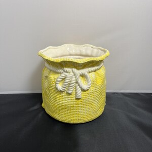 May include: A yellow ceramic planter shaped like a burlap sack with a white rope tied around the top.