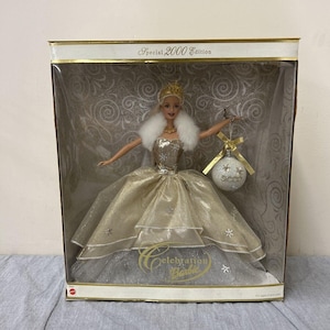 May include: A Special 2000 Edition Barbie doll in a display box. The doll wears a gold and silver gown, a white fur stole, and a golden crown. She holds a decorative ornament. The box has the words "Celebration Barbie".