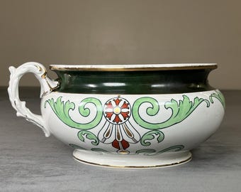 May include: White ceramic bowl with a green and gold rim, a green band, and a decorative floral design in red, white, and gold. The bowl has a white handle with gold accents.