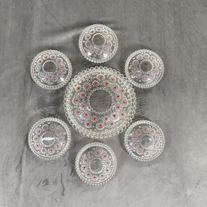 Peut inclure: Un ensemble de service en verre transparent composé d'un grand plat rond et de six petites assiettes assorties. Chaque pièce présente un motif floral texturé avec de petits accents circulaires rouge vif incrustés au centre des fleurs.
