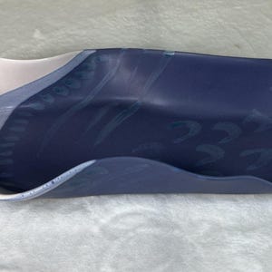 May include: A ceramic serving dish with a wavy rim. The dish is primarily navy blue, with a section of light blue and white. The interior has a pattern of small, light-coloured shapes. The dish is approximately 36 cm long.