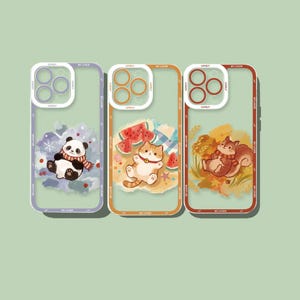 Puede incluir: Tres fundas transparentes para teléfono con protector de lente. La izquierda muestra un panda con bufanda, la central un gato con sandía y la derecha una ardilla entre hojas de otoño. Cada funda incluye el texto impreso MY LOVER.