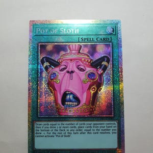 Könnte beinhalten: Eine holografische Yu-Gi-Oh!-Sammelkarte mit dem Titel Pot of Sloth, eine Zauberkarte, die einen rosafarbenen, anthropomorphen Topf mit weit geöffnetem Mund, dunklen Griffen und goldenen Akzenten zeigt. Der Kartentext beschreibt die Spielregeln.
