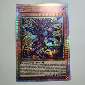 Puede incluir: Una carta coleccionable holográfica de Yu-Gi-Oh! titulada Black Chaos, que muestra una figura con armadura oscura, cabello puntiagudo y un bastón. La carta presenta el texto Spellcaster/Effect, ATK/3000, DEF/2500 y un icono de atributo morado.