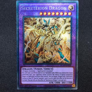 Puede incluir: Una tarjeta coleccionable holográfica con "Secreterion Dragon". La tarjeta tiene un borde púrpura y una ilustración detallada de una criatura parecida a un dragón en oro, azul y blanco. El texto de la tarjeta incluye ATK/3000 DEF/1500.