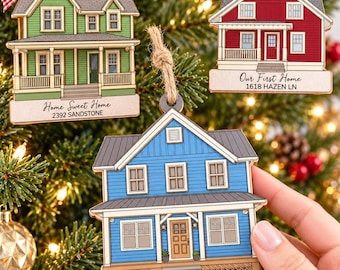 May include: Three wooden house-shaped ornaments with twine hangers. One green with 'Home Sweet Home 2392 SANDSTONE', one red with 'Our First Home 1618 HAZEN LN', and one blue with 'Our First Home 148 WILSON ST' printed on the base.
