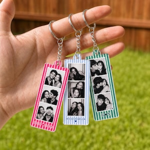 May include: Three rectangular acrylic keychains with metal rings and chains. Each features vertical stripes in pink, light blue, or green, and contains three black and white photo strips. Text includes names David and Emma, Besties Forever, and K S.