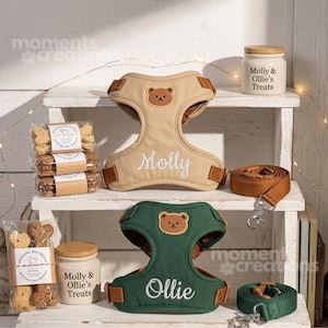 May include: A beige dog harness with a bear patch and the name Molly, a green dog harness with a bear patch and the name Ollie, two matching leashes, two white treat jars labelled Molly & Ollie's Treats, and two packages of bone-shaped dog treats.