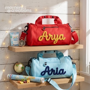 May include: Two personalised duffel bags, one red with yellow lettering reading "Arya" and one light blue with navy lettering reading "Aria", sit on wooden shelves. A compass, travel wipes, a globe, and a map are also on the shelves.