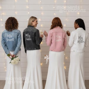 Puede incluir: Cuatro chaquetas vaqueras en azul, negro, rosa y blanco, cada una adornada con adornos de perlas en los hombros. Las chaquetas tienen los nombres "Mrs. Bennett", "Mrs. Parker", "Mrs. Carter" y "Mrs. Miller" impresos en la espalda en escritura blanca.