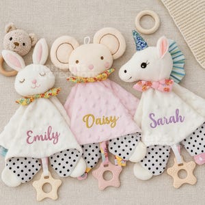 Könnte beinhalten: Drei Plüsch-Baby-Kuscheltücher in Form eines Hasen, einer Maus und eines Einhorns. Jedes hat einen gestickten Namen auf der Vorderseite: "Emily", "Daisy" und "Sarah". Die Kuscheltücher haben gepunktete Unterteile und sternförmige Beißringe.