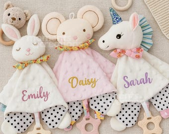 May include: Three plush security blankets featuring a rabbit, a mouse, and a unicorn. The rabbit is embroidered with the name Emily, the mouse with Daisy, and the unicorn with Sarah. Each blanket has a textured fabric, a patterned base, and a star-shaped wooden teether attached.