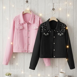 K&ouml;nnte beinhalten: Zwei Jeansjacken, eine rosa und eine schwarze, h&auml;ngen vor einer wei&szlig;en Holzpaneelwand. Beide Jacken haben lange &Auml;rmel, eine Knopfleiste und sind mit wei&szlig;en perlenartigen Perlen verziert. Die rosa Jacke ist links, die schwarze Jacke rechts.